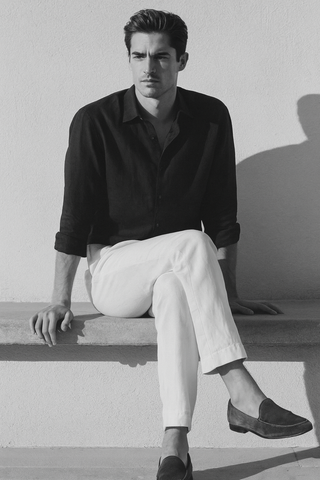 Man wearing a black shirt and white pants sitting against a light background
