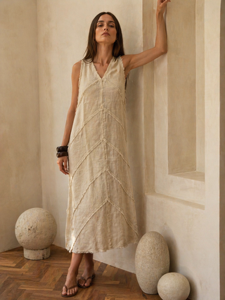 Woman in a beige dress standing against a neutral wall with decorative stones on the floor.